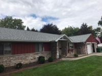 A house with a gray roof and a red door is sitting on top of a lush green lawn.