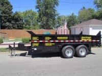 A dump trailer is parked on the side of the road in front of a house.