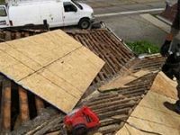 A man is cutting a piece of plywood on a roof.