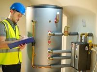 A man is standing in front of a water heater and writing on a clipboard.