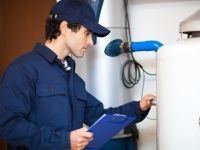 A man is holding a clipboard and looking at a water heater.