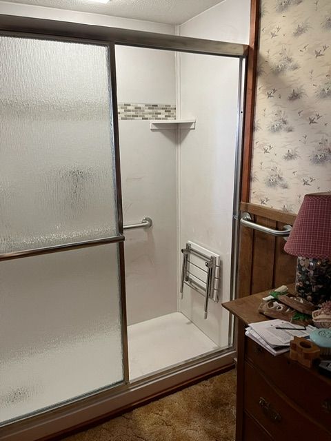 A bathroom with a sliding glass shower door and a chair in it.