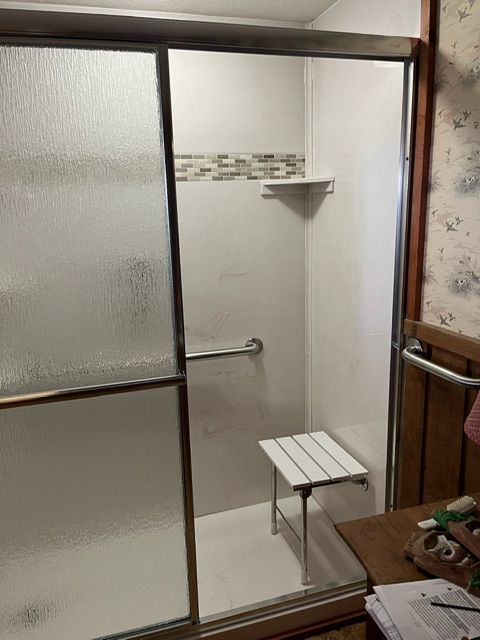 A bathroom with a sliding glass shower door and a bench.