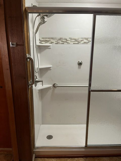 A shower with a sliding glass door and a hand rail.