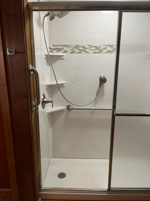A shower stall with a sliding glass door and a hand rail.