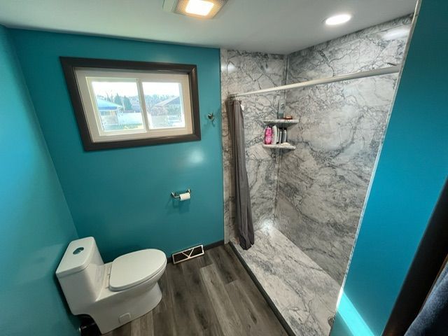 A bathroom with a toilet , shower and window.