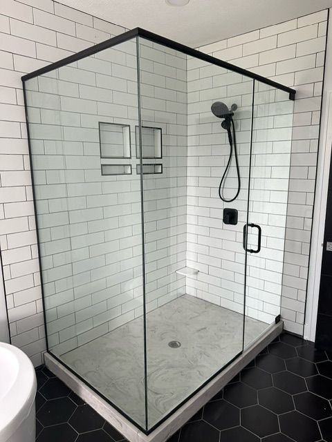A shower stall with a black frame and white tiles in a bathroom.