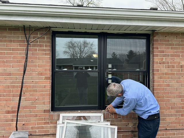 A man is fixing a window on a brick house.
