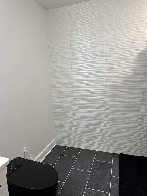 A bathroom with a black toilet and a white wall.