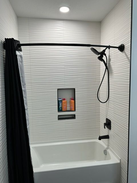 A white bathtub with a black shower curtain and a shower head