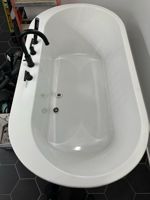 A white bathtub with black faucets is sitting on a black tiled floor.