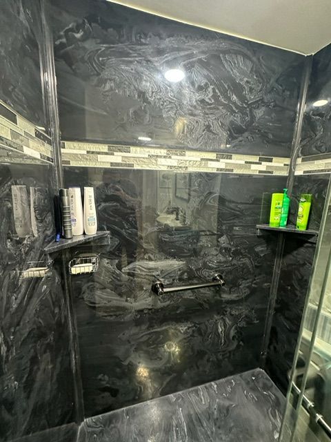 A bathroom with a black tiled wall and a walk in shower.