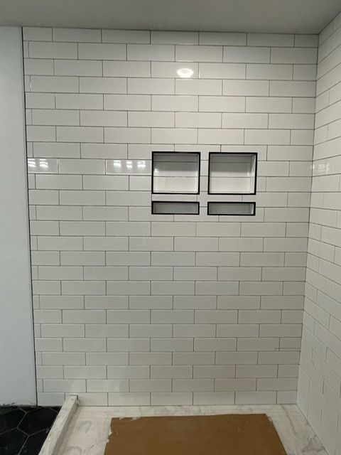A bathroom with white tiles and two shelves in the shower.