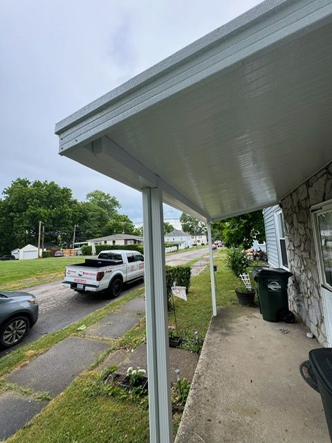 A white truck is parked on the side of the road under a porch.
