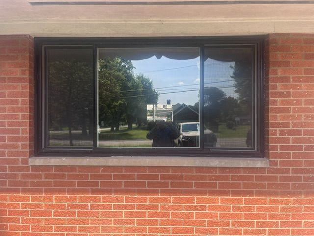 A large window on a brick building with a reflection of trees in it.