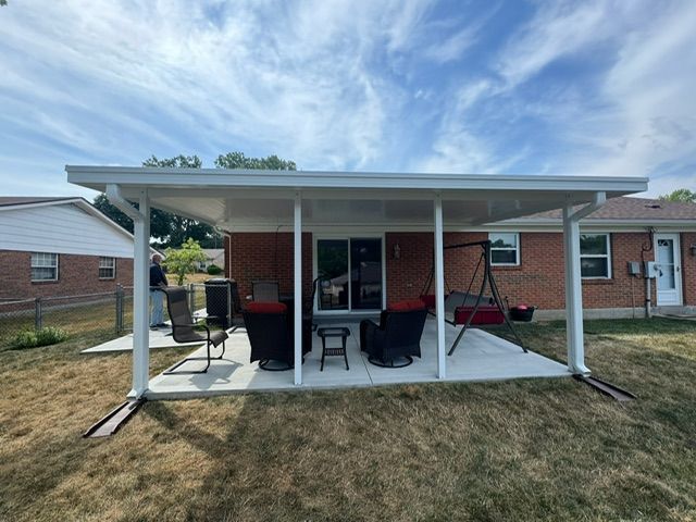 The backyard of a brick house with a covered patio with chairs and a swing.