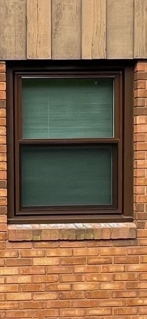 A window on a brick building with a brown frame and green blinds.