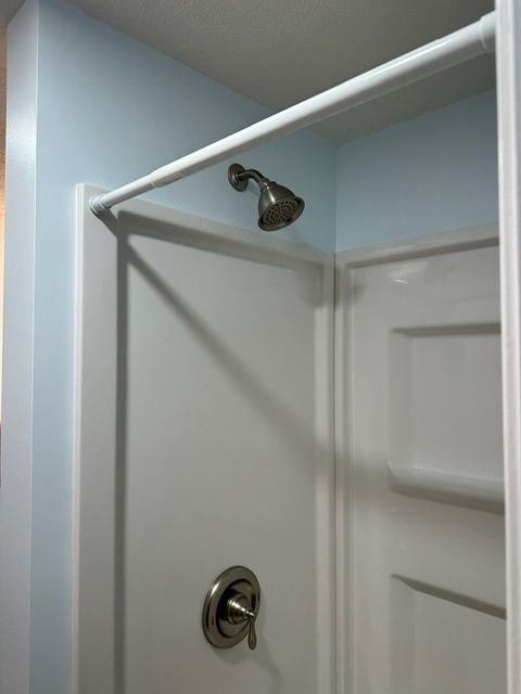 A shower head hangs over a white door in a bathroom