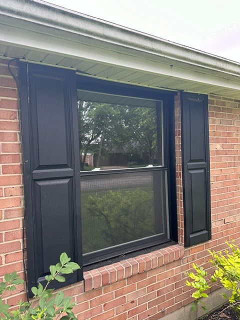 A window with black shutters on a brick house.
