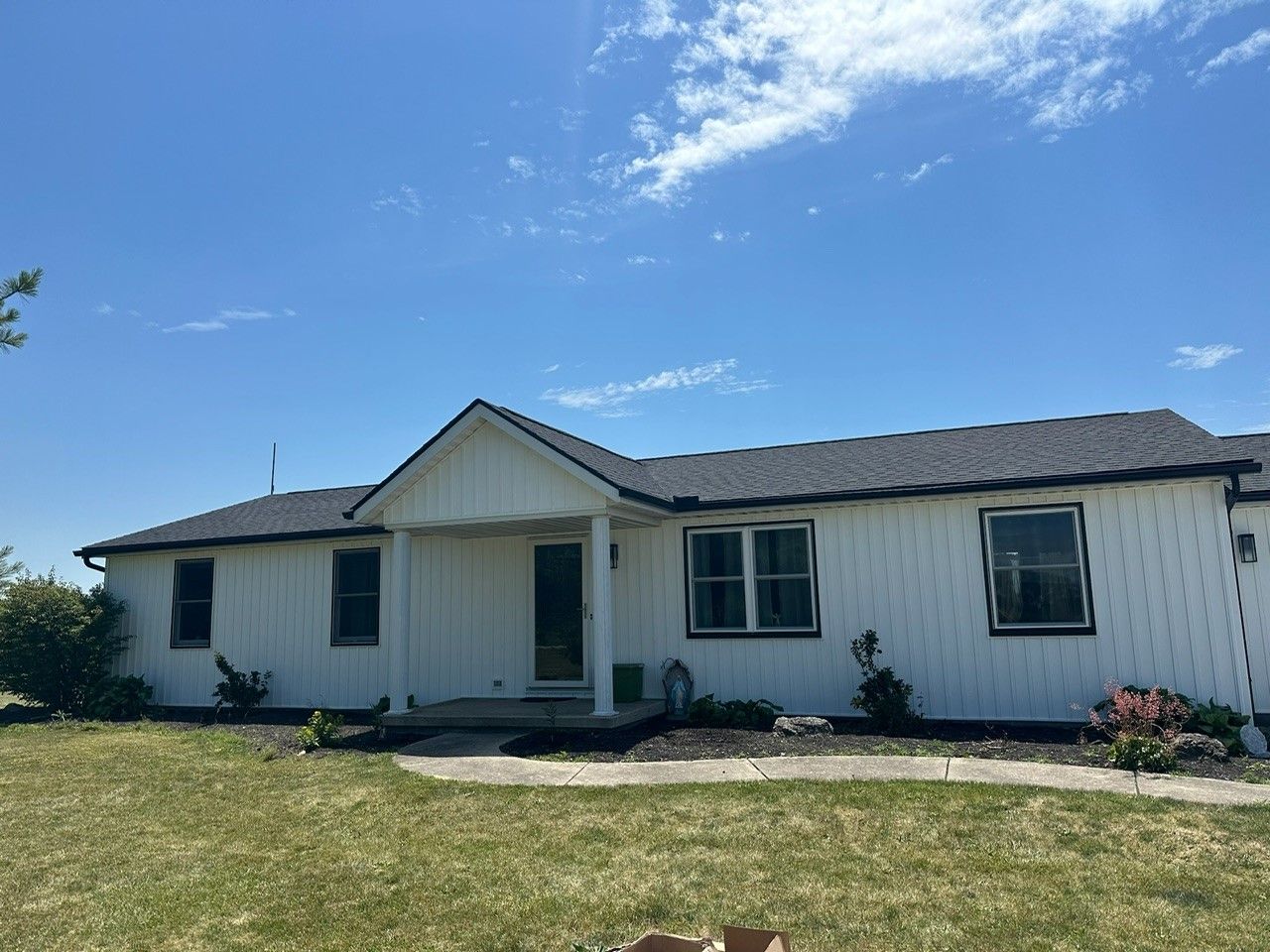 A white house with a gray roof is sitting on top of a lush green field.