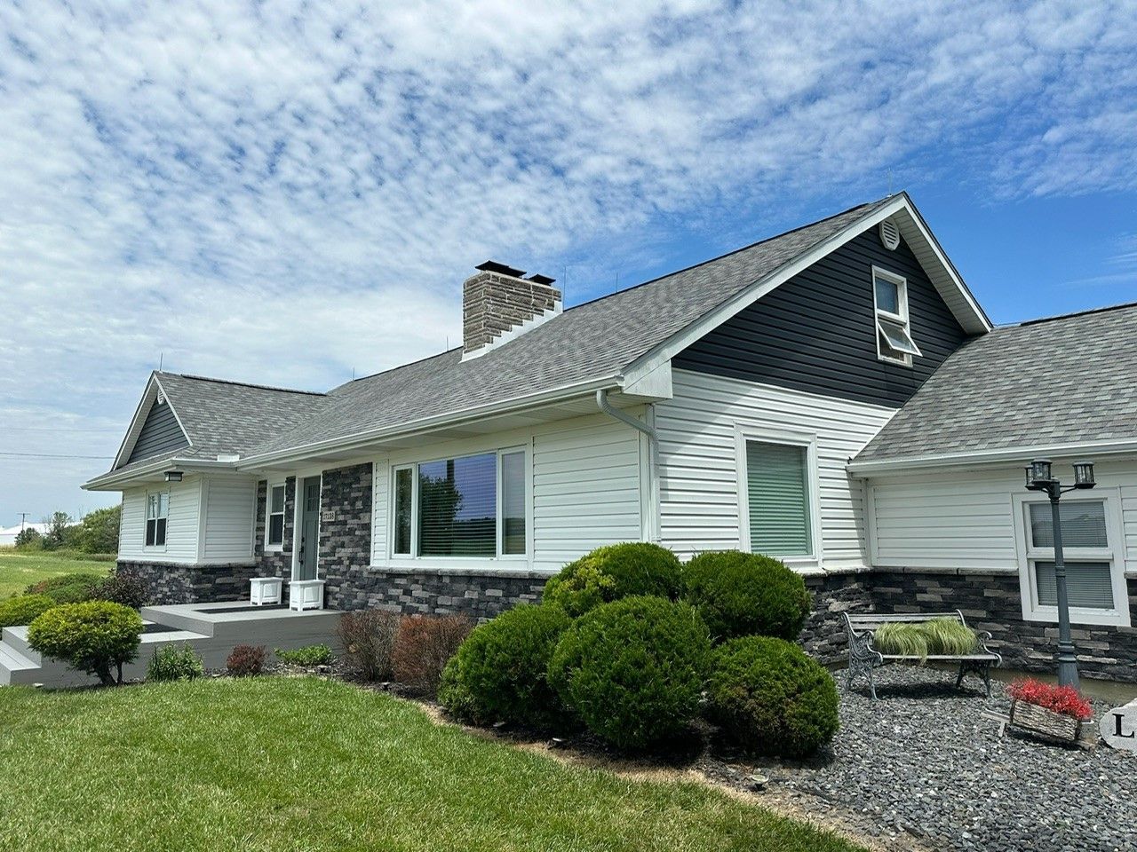 A large white house with a gray roof is sitting on top of a lush green field.