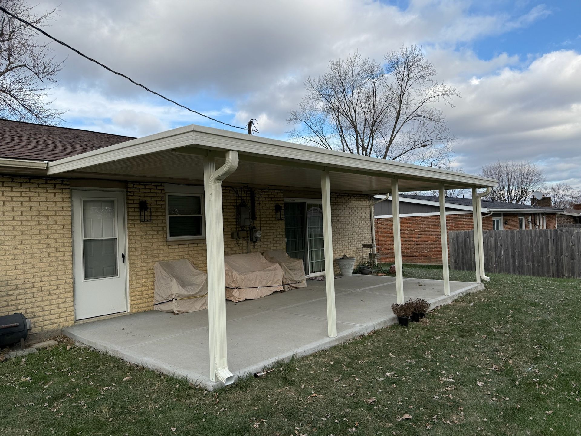 A covered patio with a picnic table and chairs in the backyard of a house.