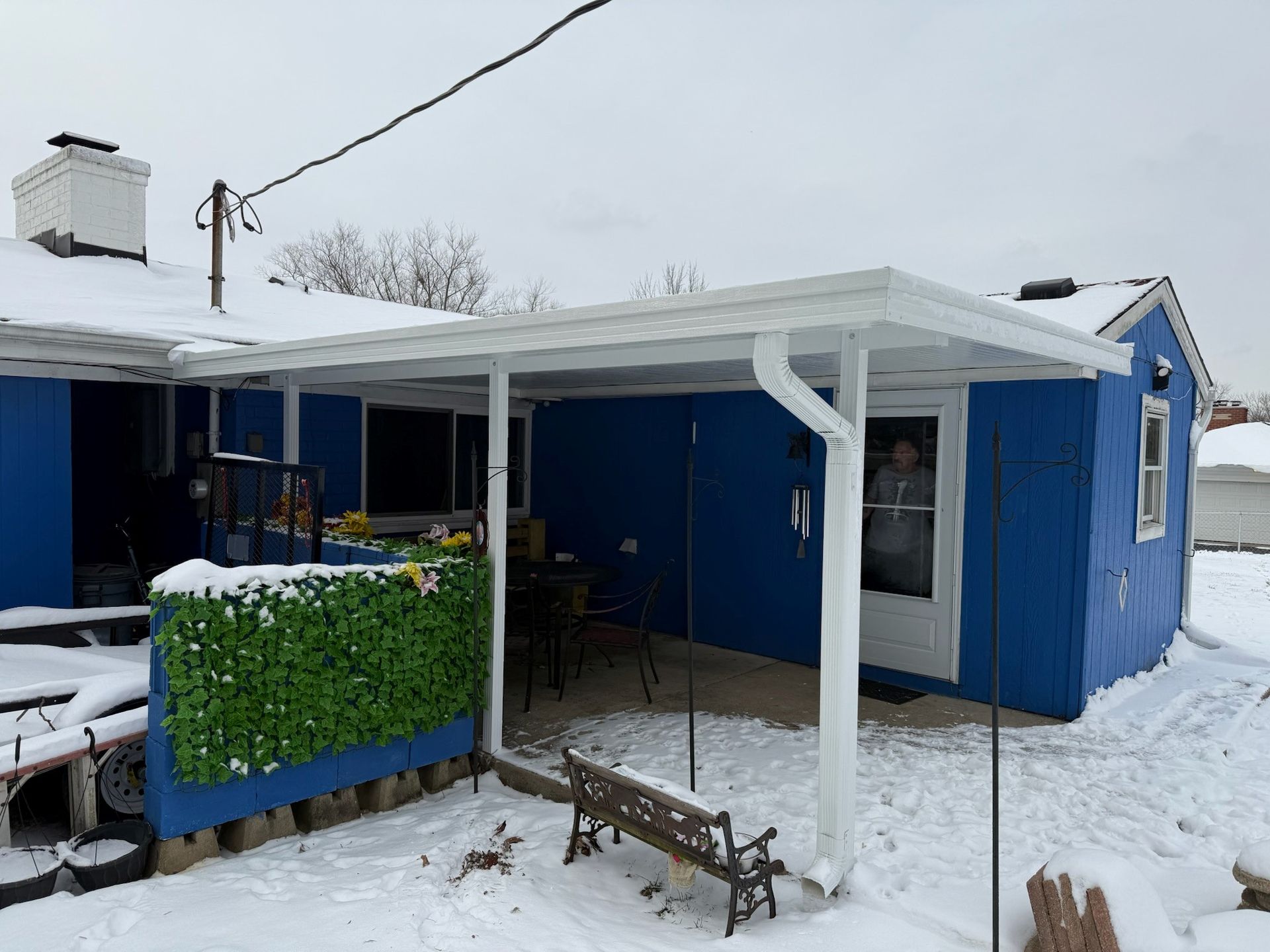 A blue house with a white porch and a bench in the snow.