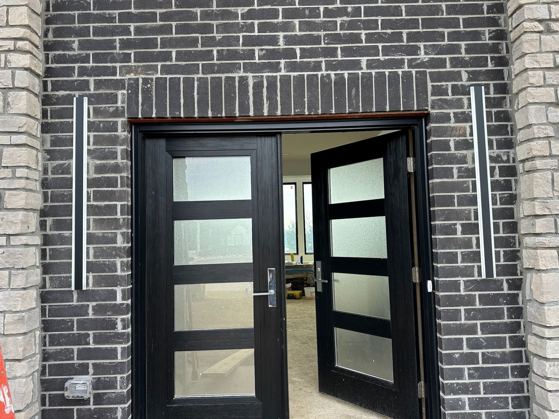 A black door with a brick wall behind it is open to a living room.