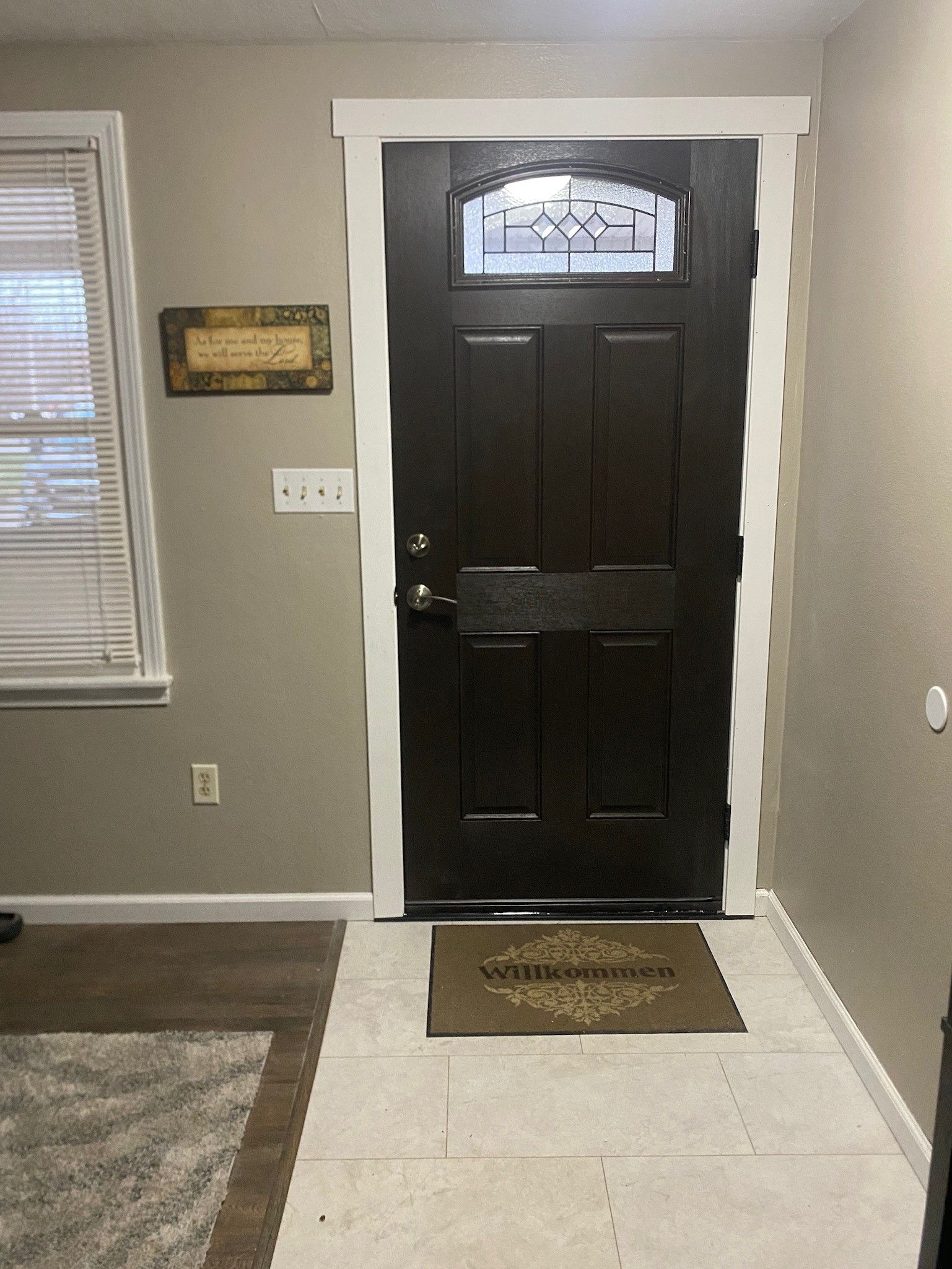 A hallway with a black door and a welcome mat.