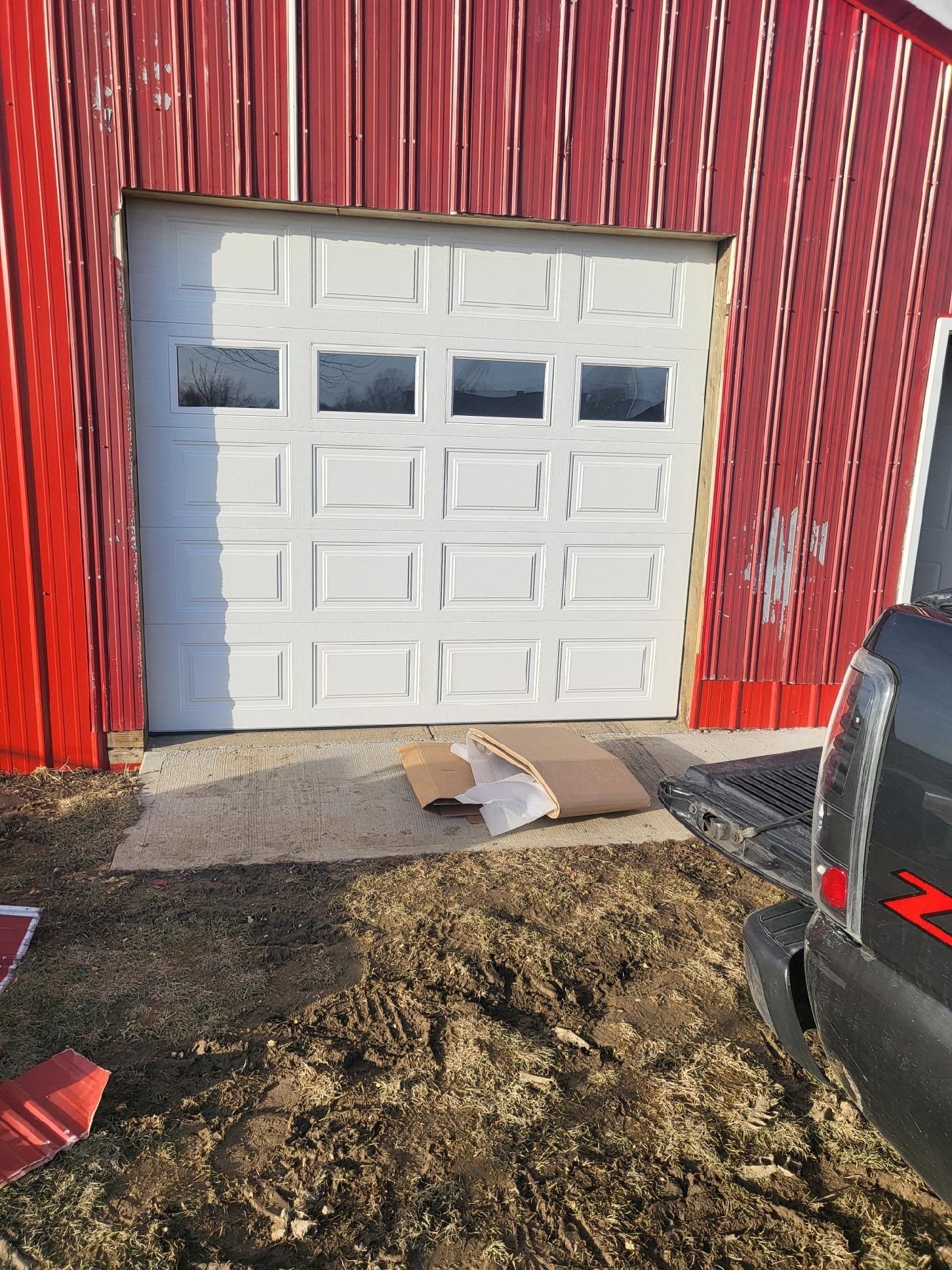 A white garage door is sitting in front of a red barn.
