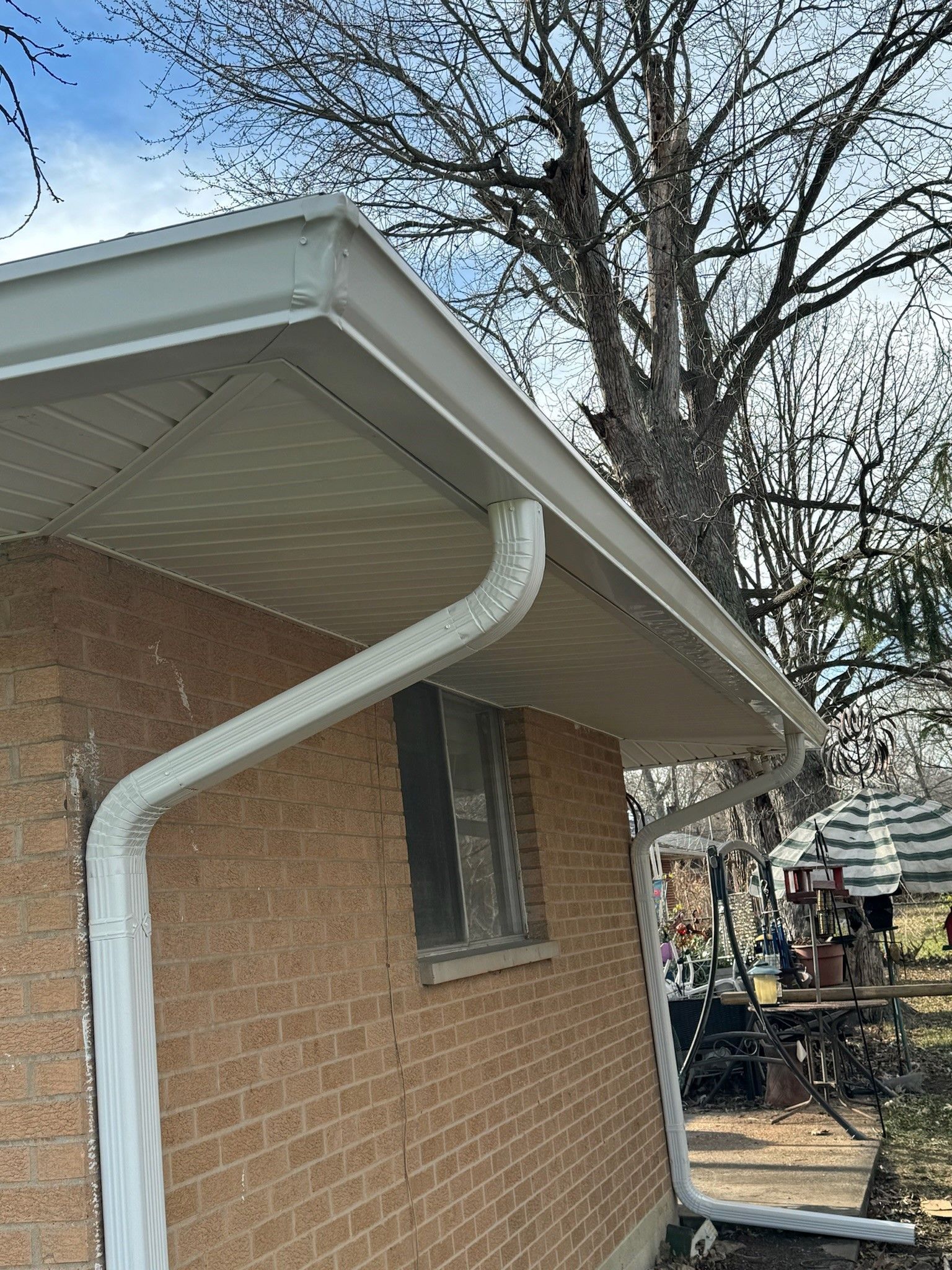 A brick house with a white gutter and a tree in the background.