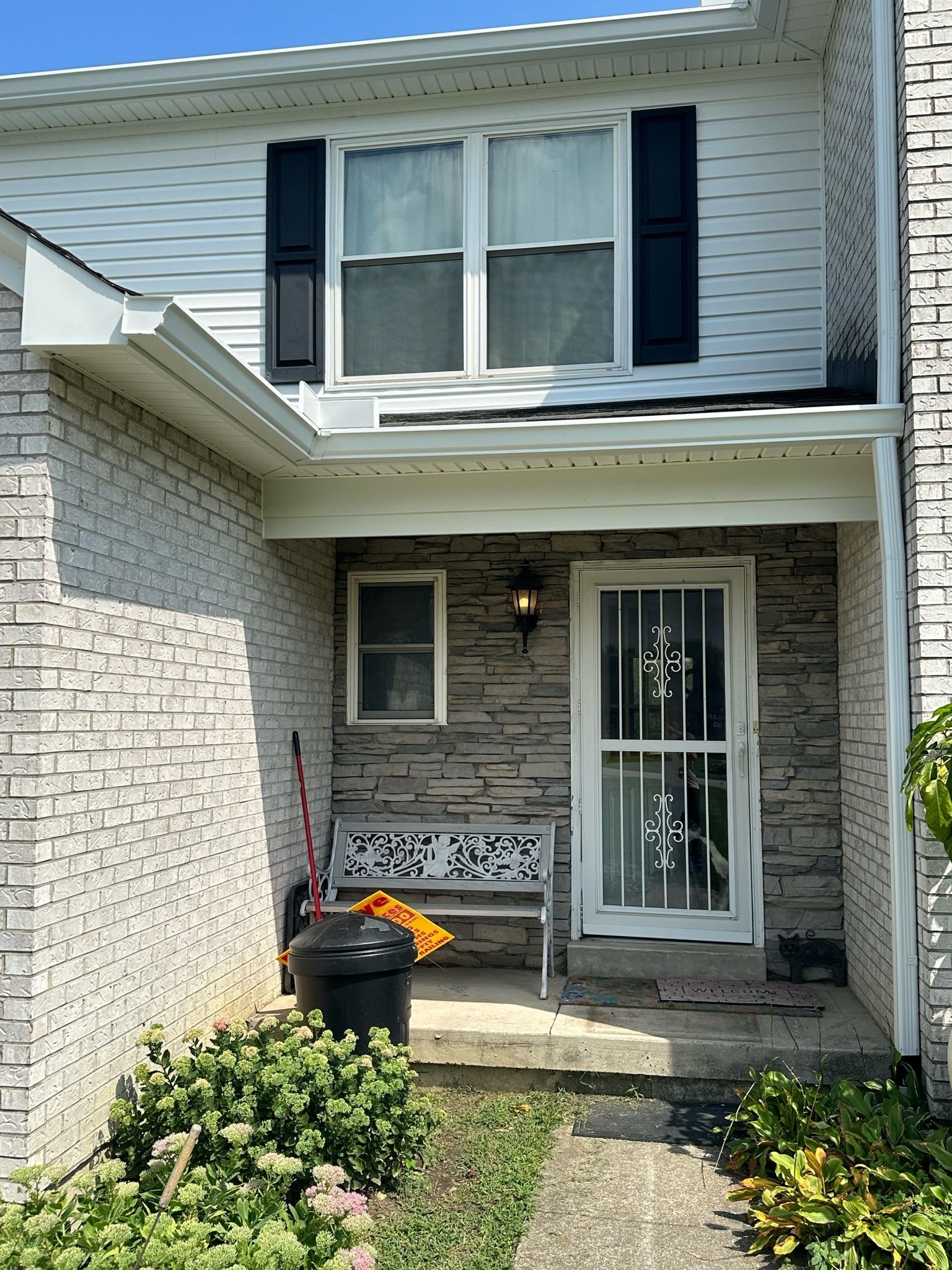A white brick house with black shutters and a porch with a bench.
