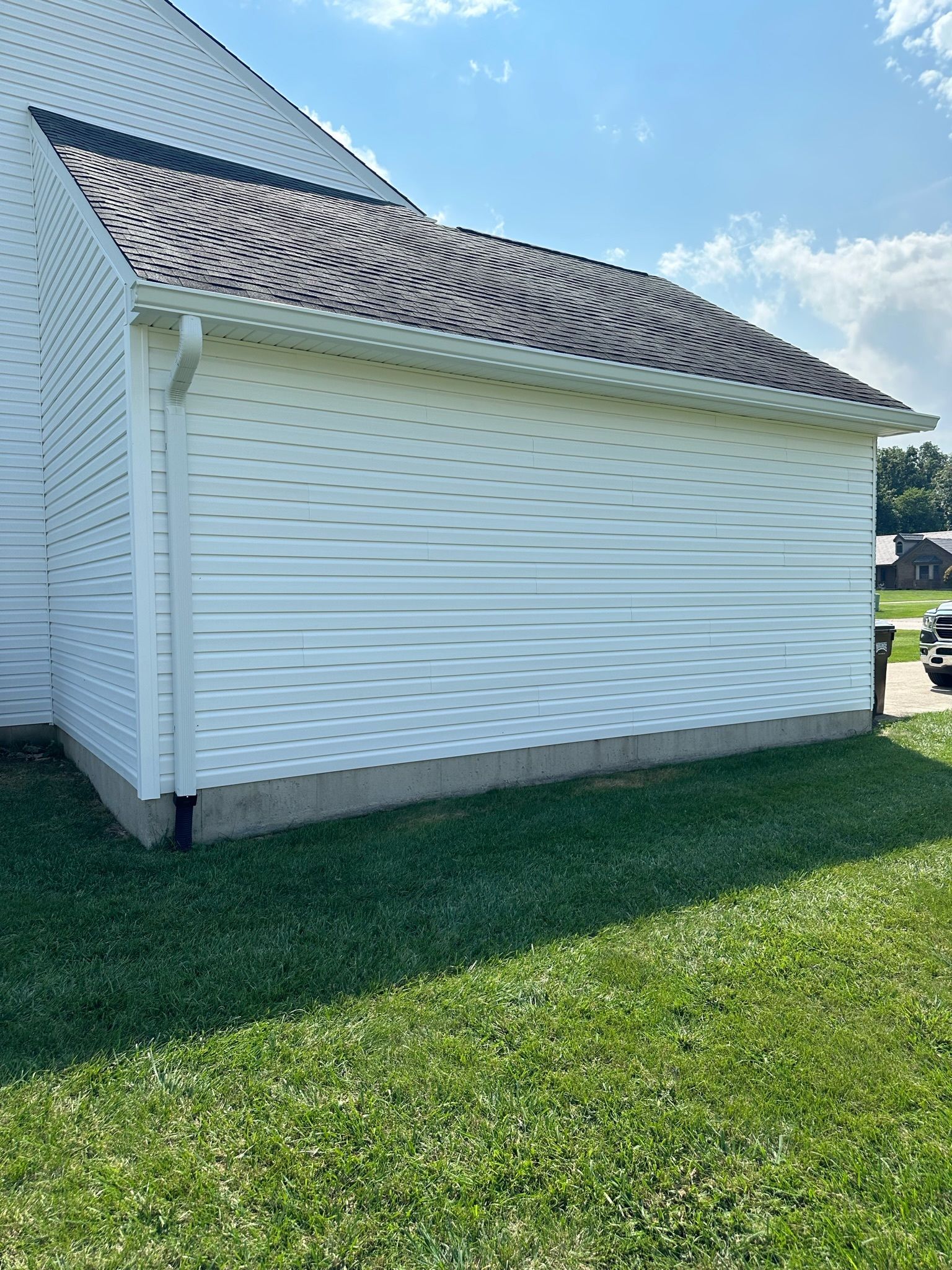 A white house with a brown roof is sitting on top of a lush green field.