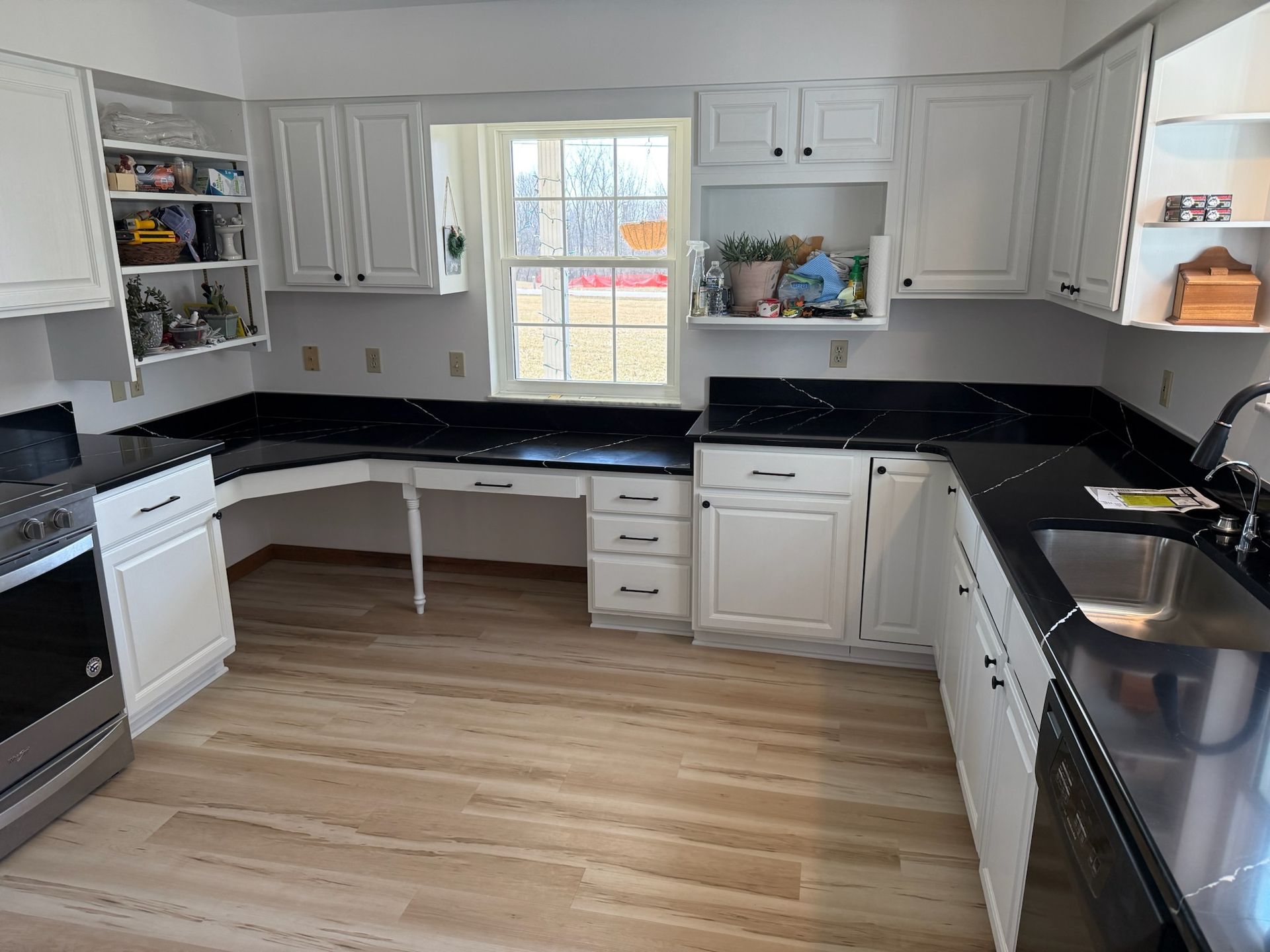 A kitchen with white cabinets, black counter tops, stainless steel appliances and a window.