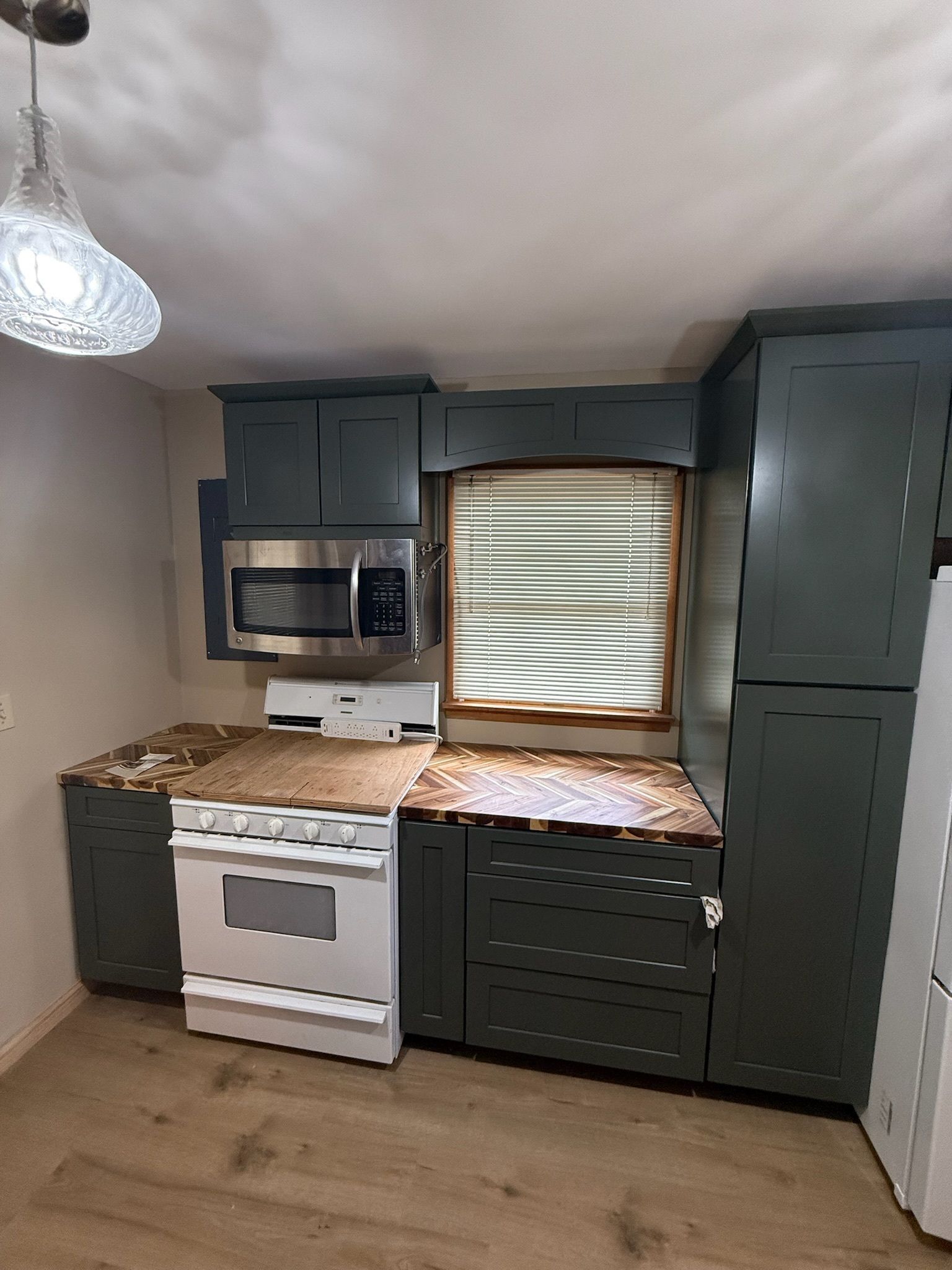 A kitchen with a stove, microwave, cabinets and a window.