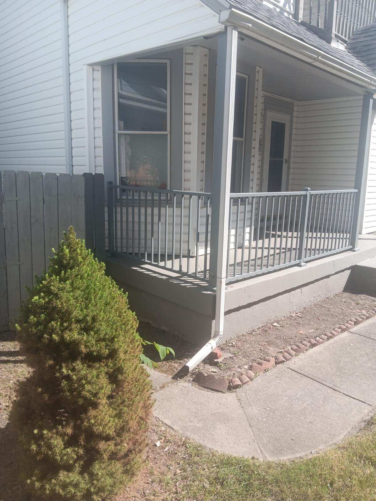 A white house with a porch and a fence in front of it.