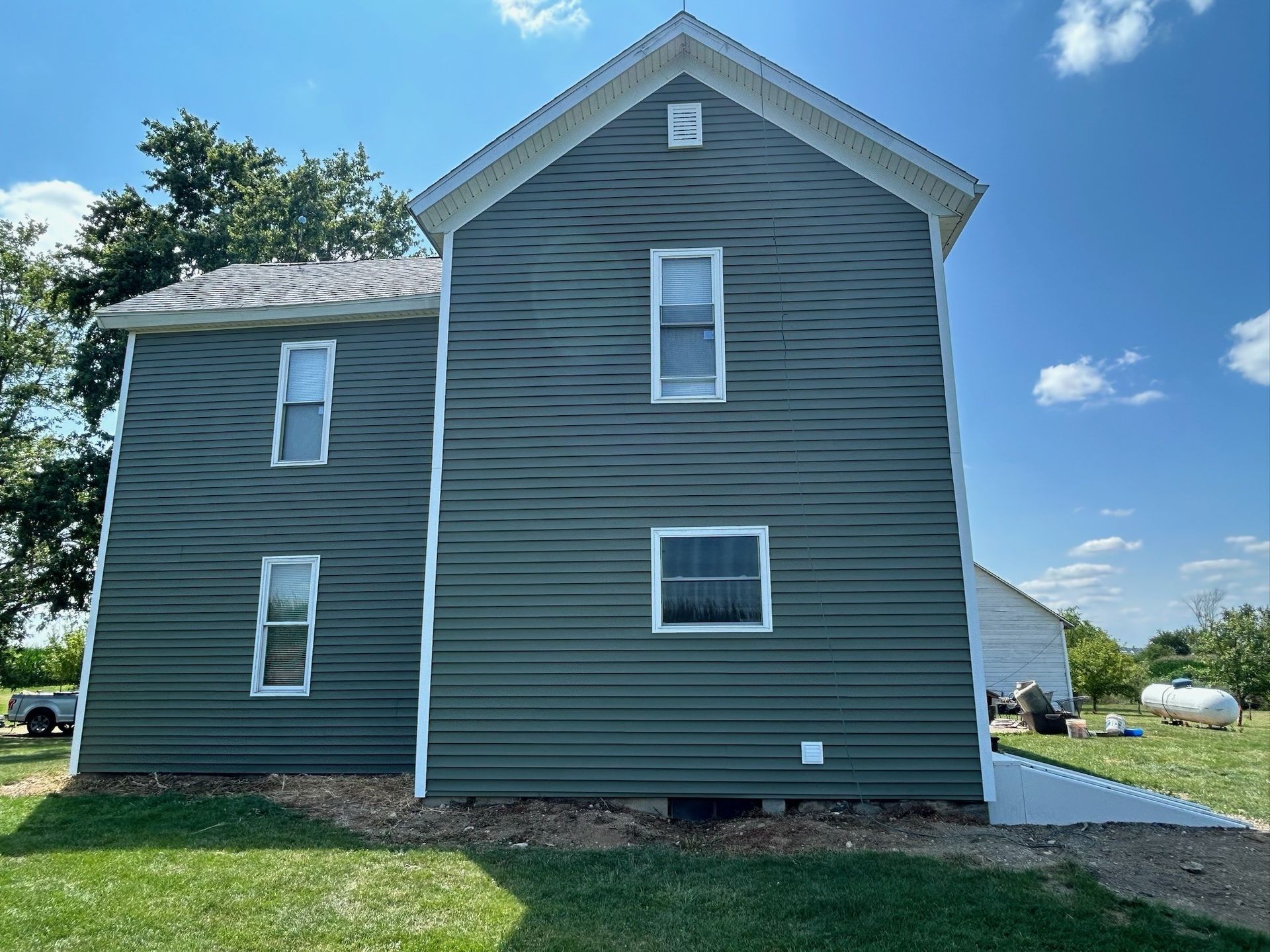 A large house with a green siding and white trim is sitting on top of a lush green field.