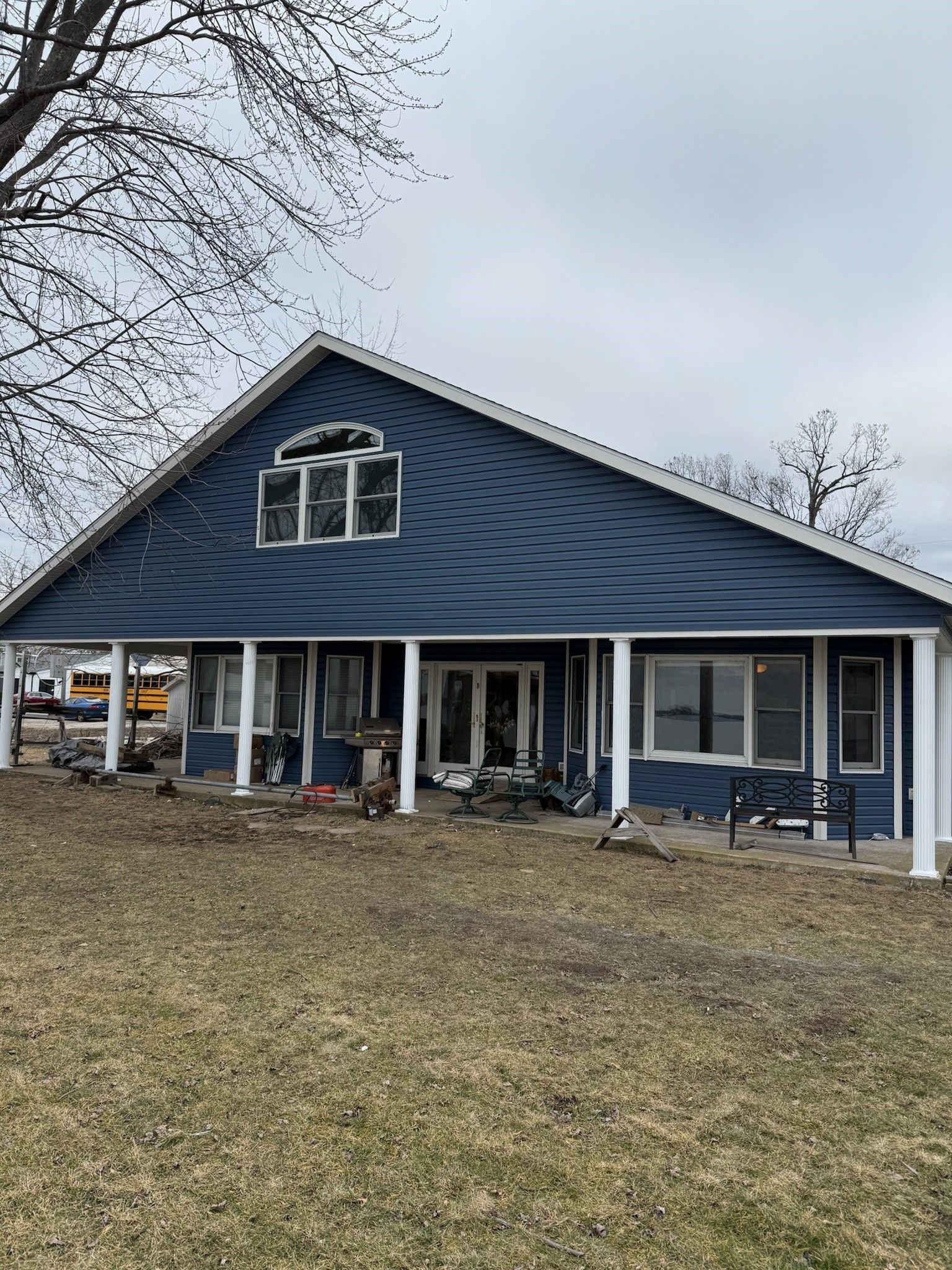 A blue house with a white porch is sitting next to a body of water.