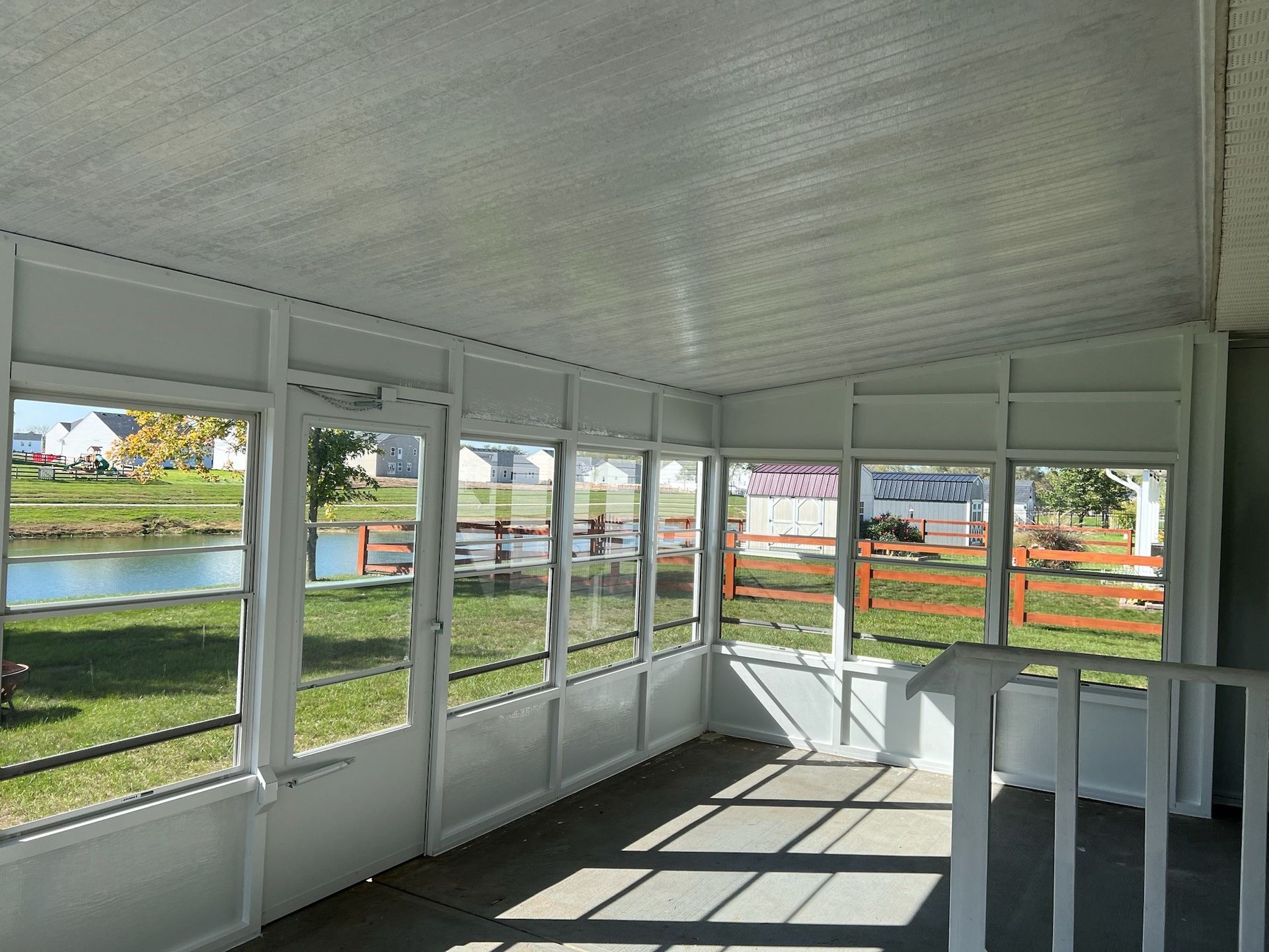 A screened in porch with a lot of windows and chairs