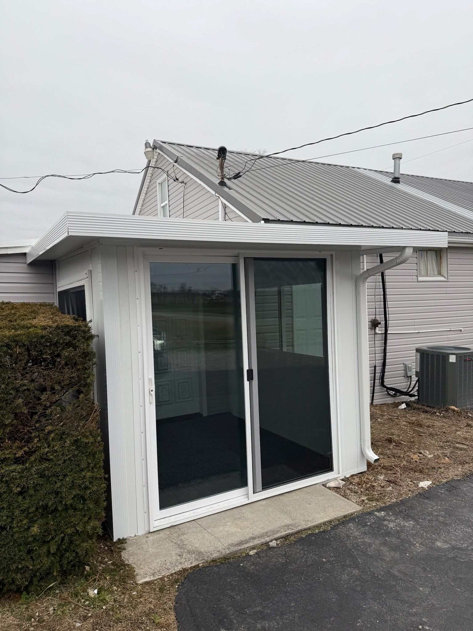 A white shed with a sliding glass door is next to a house.