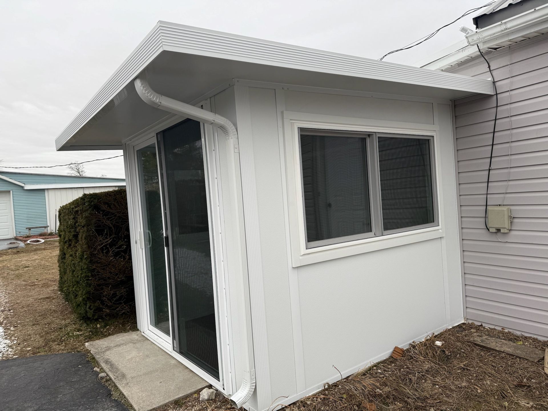 A small white shed with a roof and a window on the side of a house.