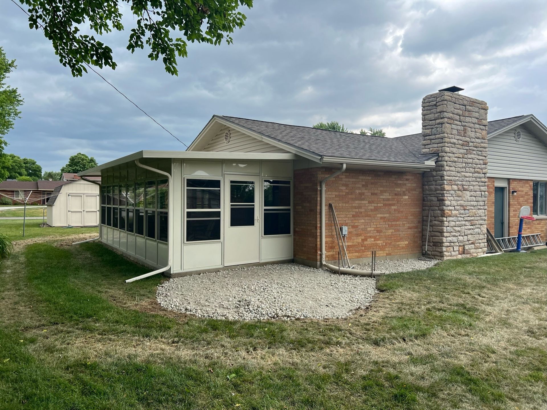 The back of a house with a screened in porch and a brick chimney.