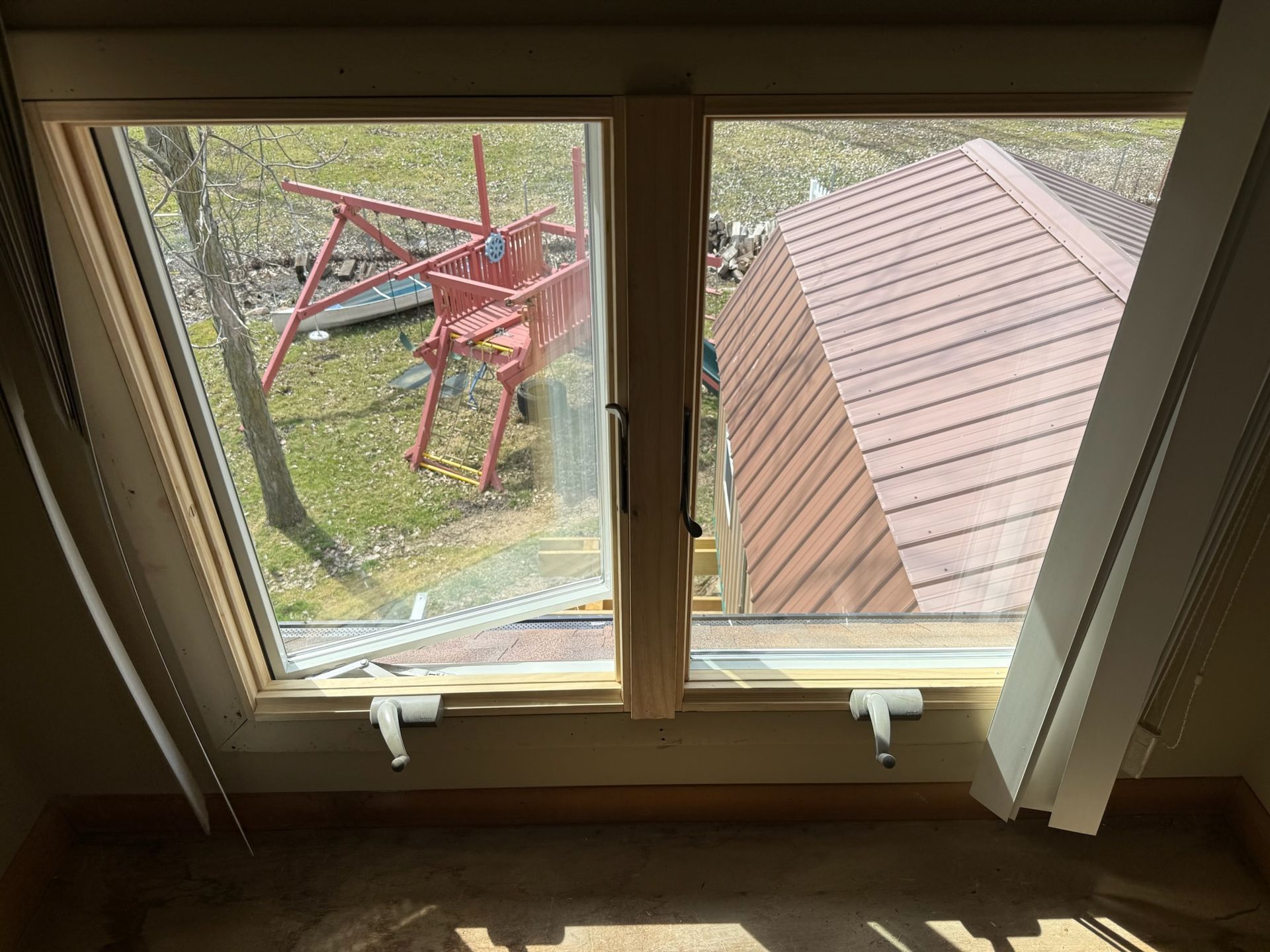 A window with a view of a shed and a red chair in the background.