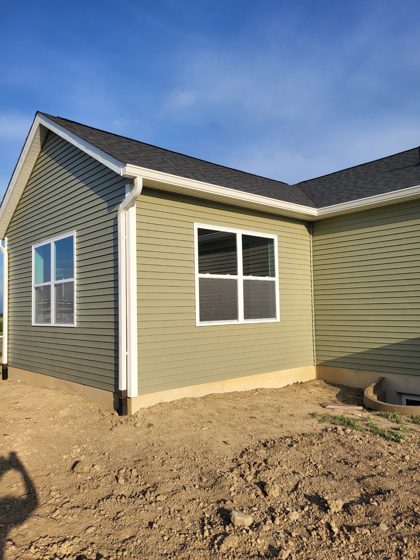 A green house with two windows is sitting on top of a dirt field.