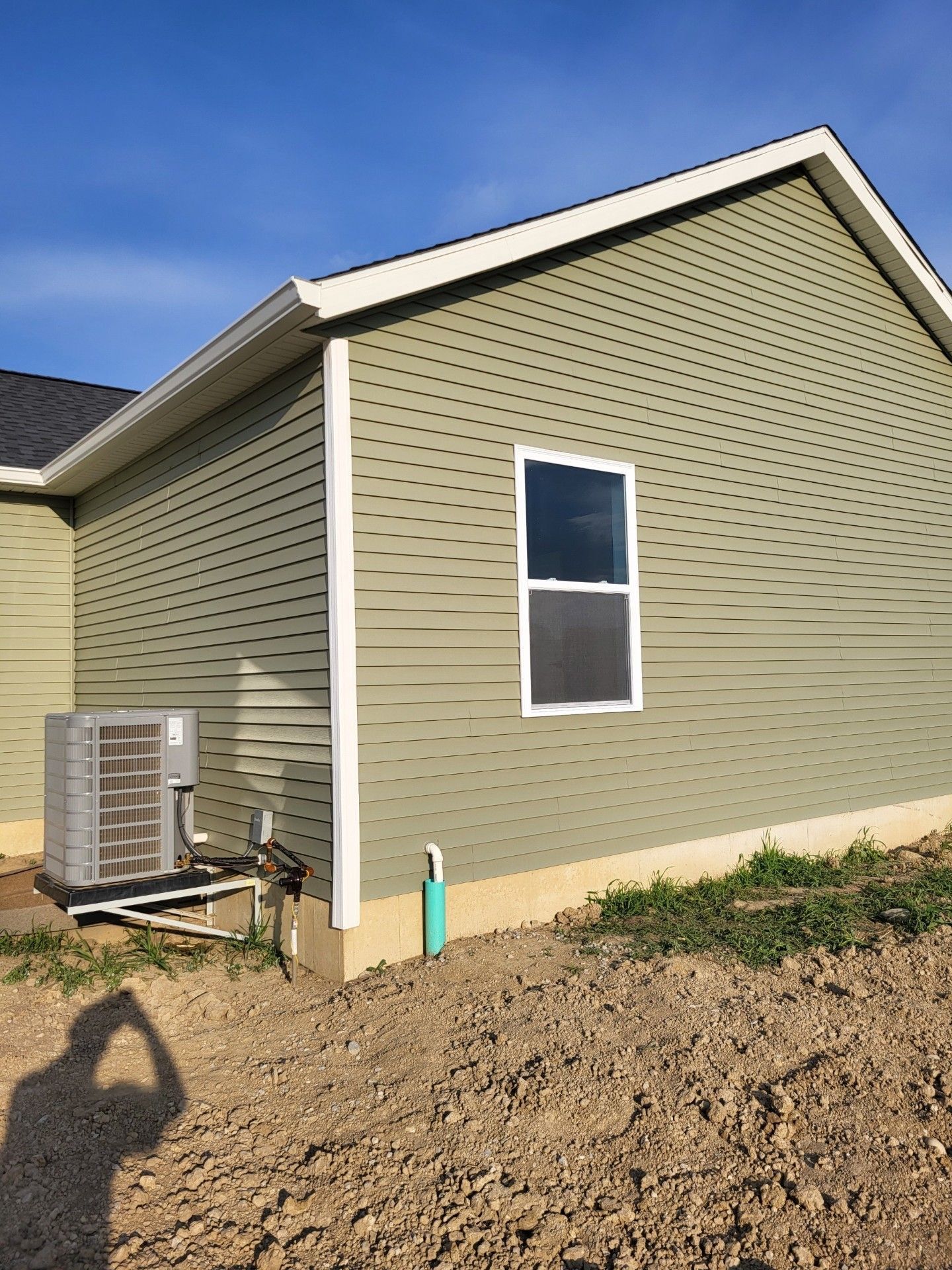 A house with a green siding and a window is sitting on top of a dirt hill.