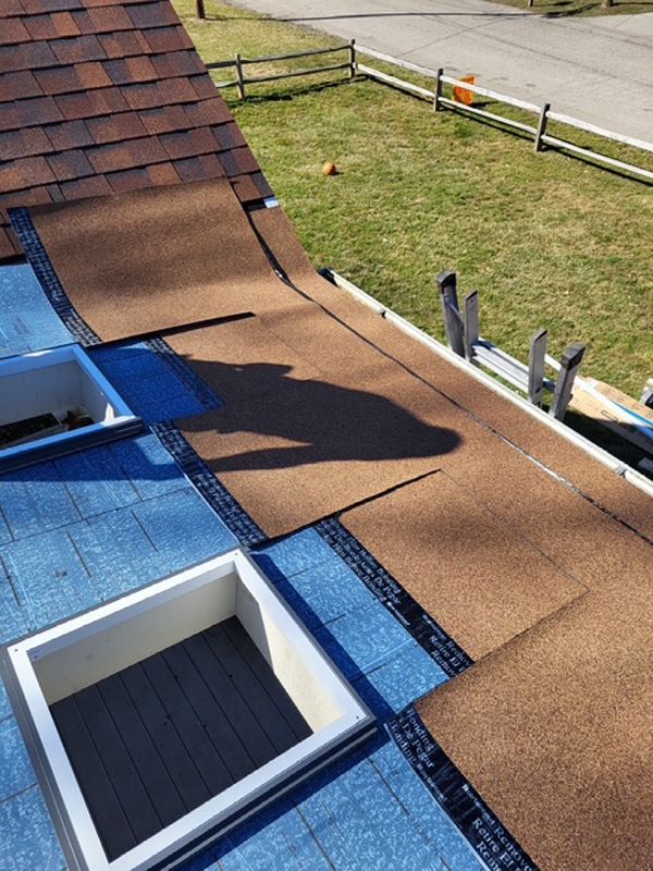 A roof with a skylight and shingles being installed on it.