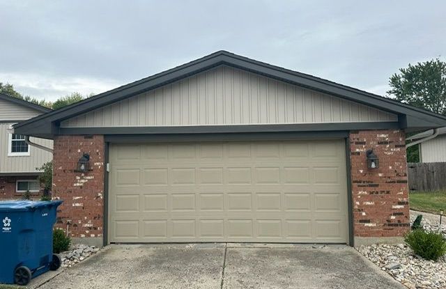 A garage door with a blue trash can in front of it.