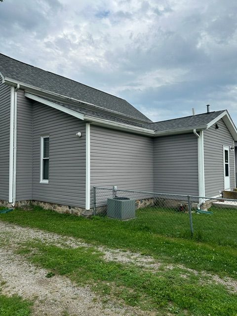 A gray house with a gray roof is sitting in the middle of a grassy field.