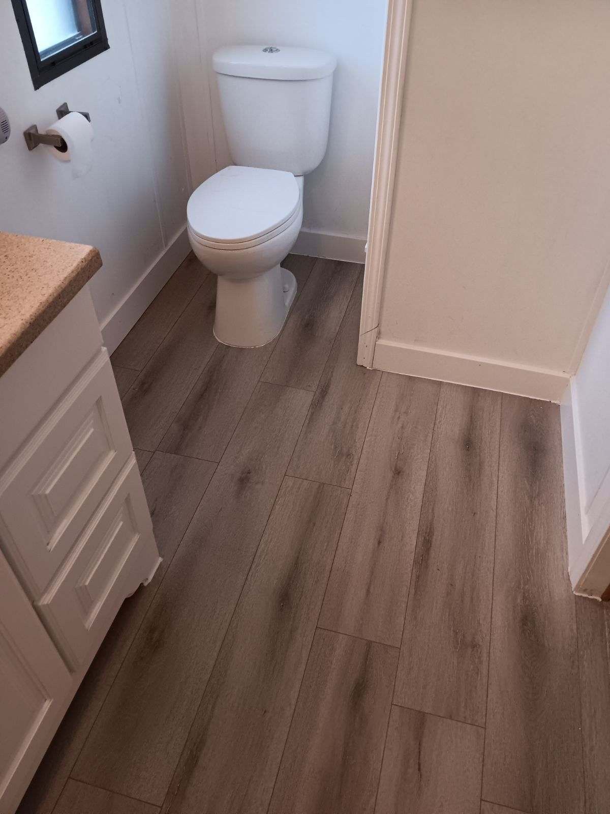 A bathroom with a toilet , sink , and wooden floor.