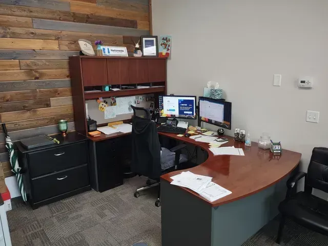 Office desk with monitors, wood wall, black chair, and storage cabinets.